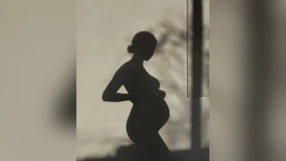 Día de spa para embarazadas: silueta de una futura mamá acariciando su panza a contraluz, en tonos cálidos, Spa Belgrano