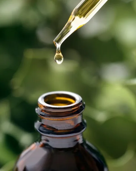 Gota de aceite esencial de tomillo cayendo de un gotero sobre fondo verde
